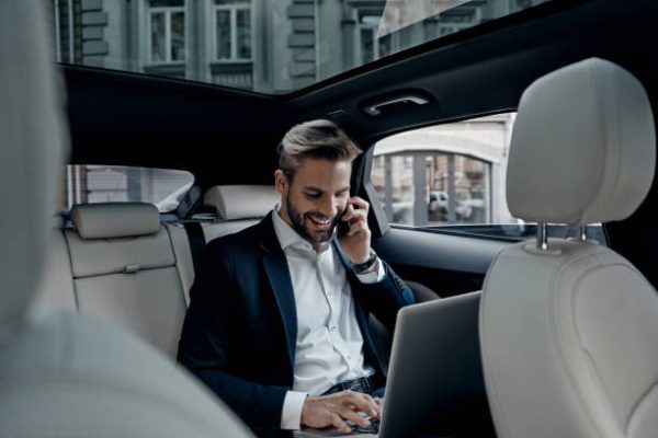 Handsome young man in full suit talking on smart phone and smiling while sitting in the car